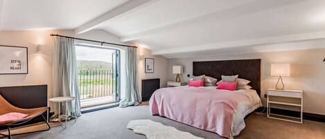 A modern bedroom with a large bed, a sofa, a small table, and a view of the outdoors.