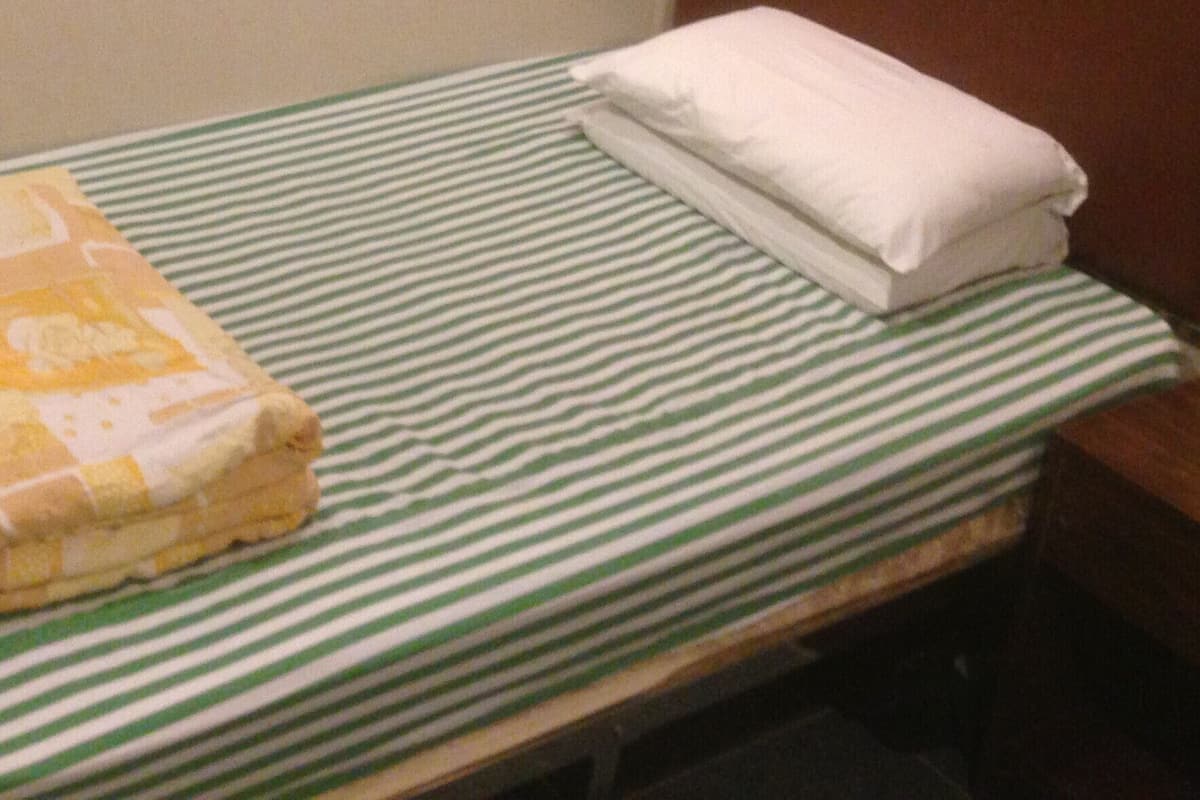 Un lit simple avec une couverture rayée verte et blanche, une couverture pliée et une serviette blanche soigneusement pliée.
