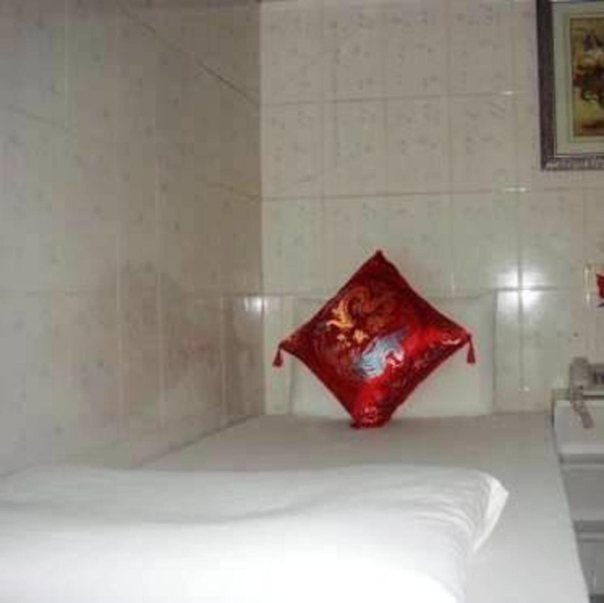 A bathroom with a white sink, a mirror, and a red decorative pillow on the floor.