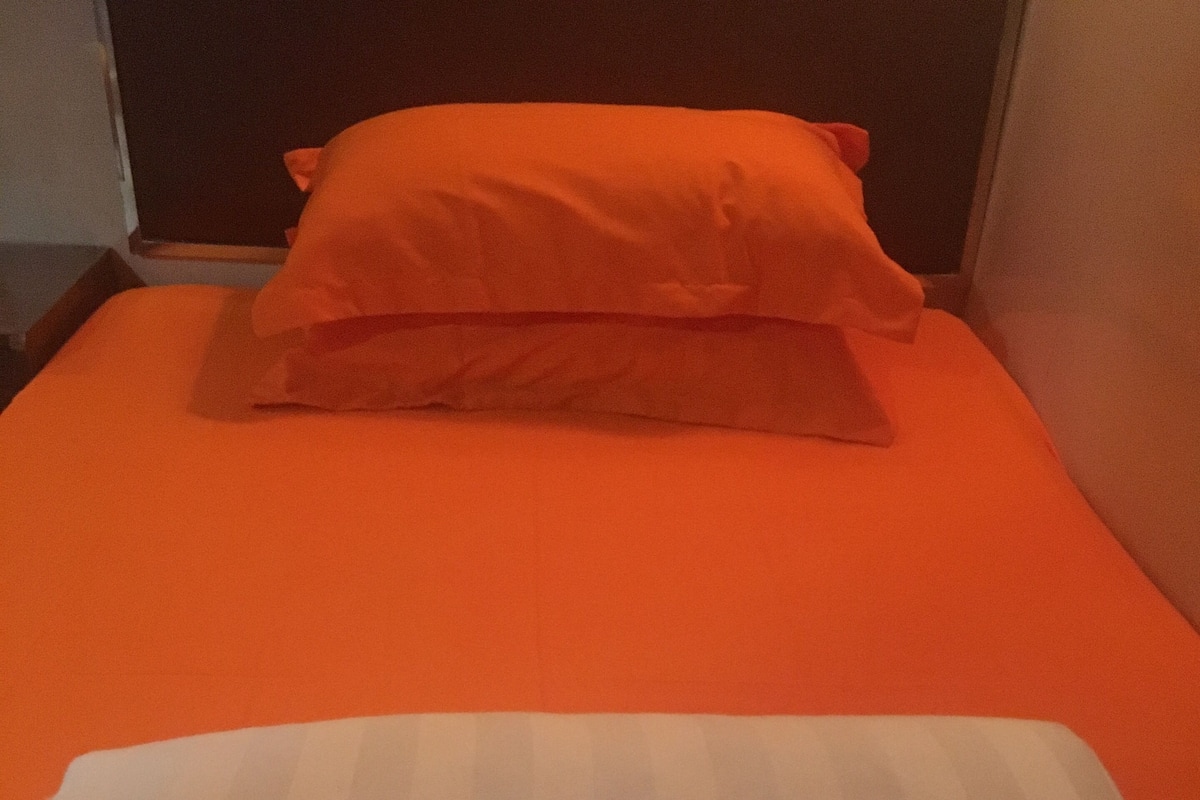 Un lit avec une couverture orange et un oreiller blanc.