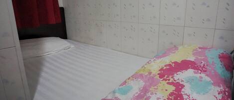 Ein kleines Zimmer mit einem Einzelbett, einer weißen Matratze und einer bunten Decke.
