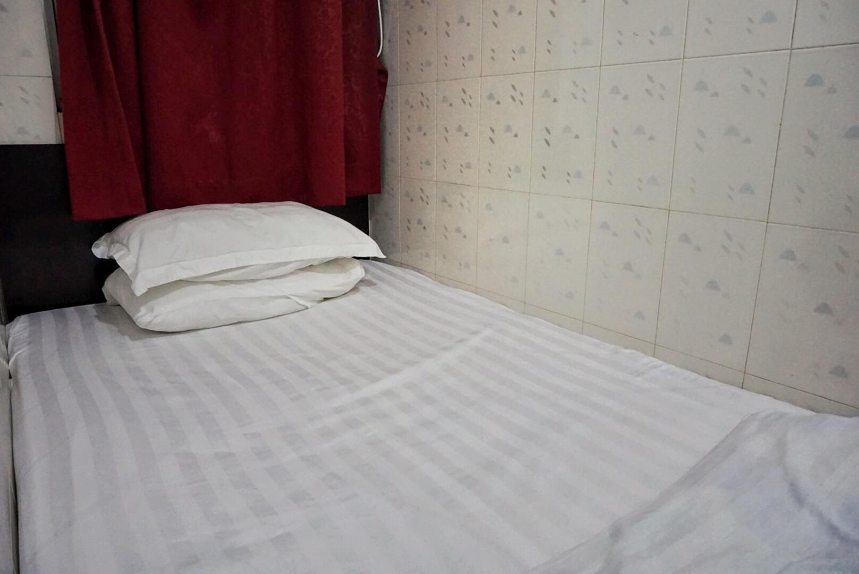 A neatly made bed with white bedding and a red curtain in the background.