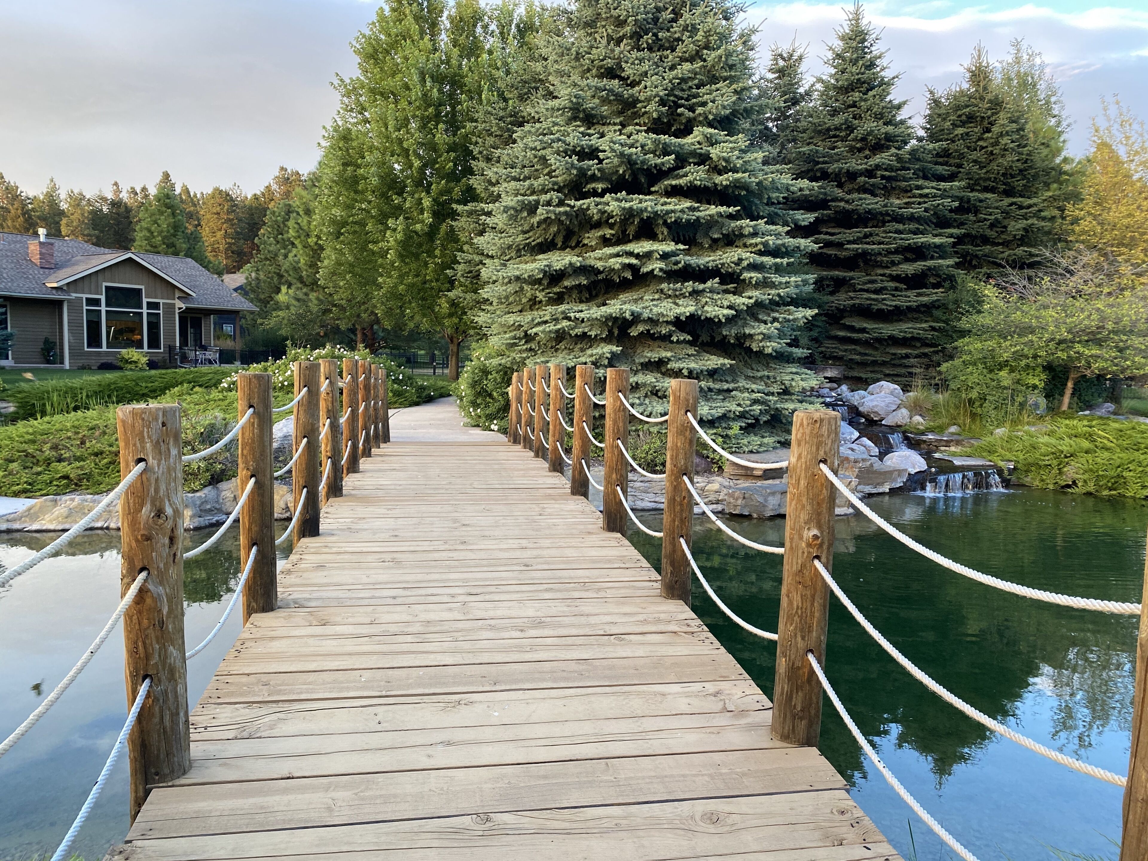 A wooden bridge with rope railings leading to a house with a visible porch.