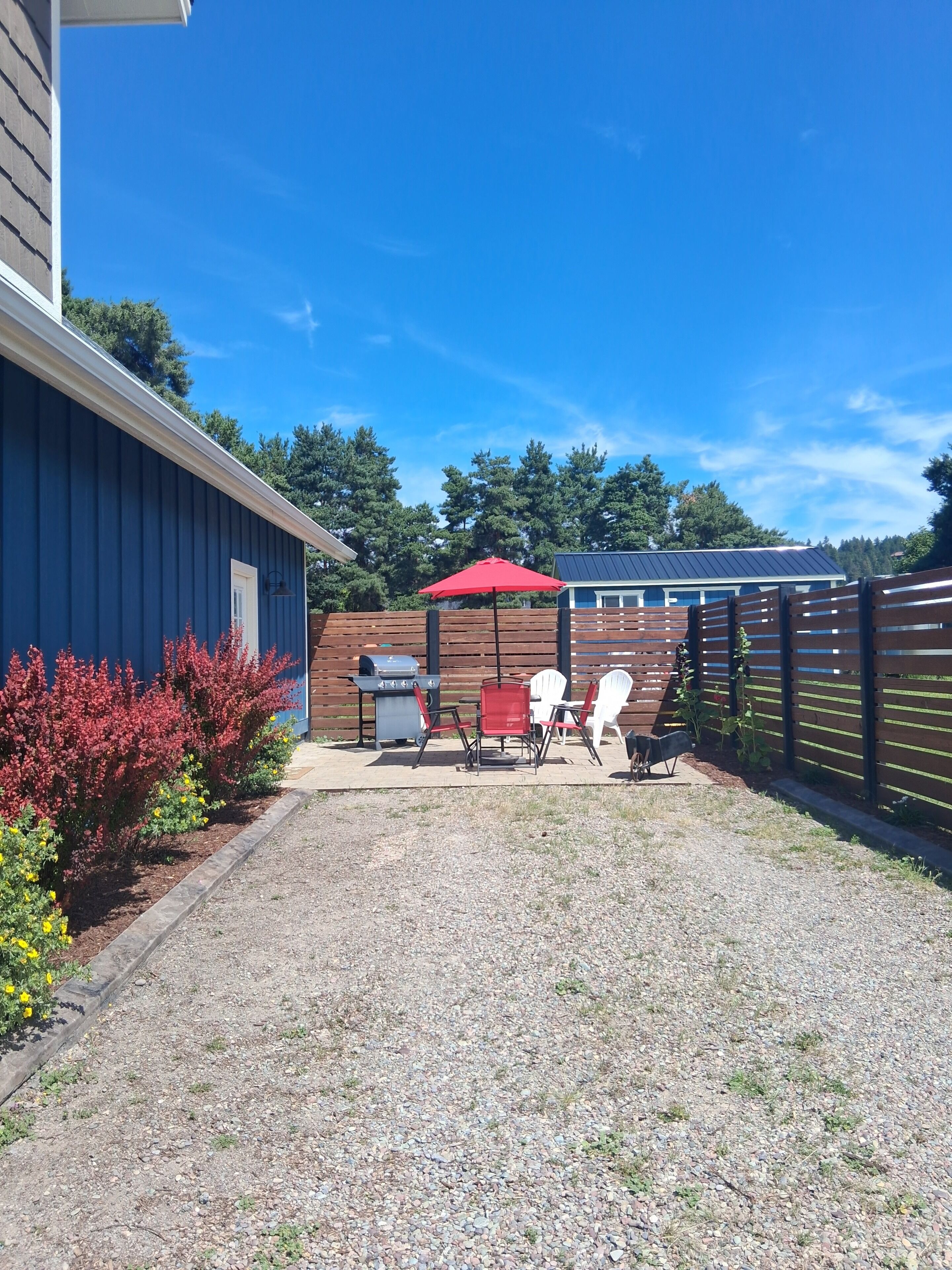 A backyard with a barbecue grill, red and white chairs, and a red umbrella.