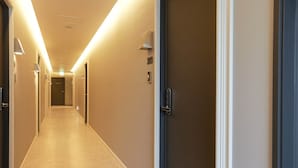 Un couloir d’hôtel avec un sol recouvert de moquette, des portes sur le côté droit et des luminaires fixés au mur.