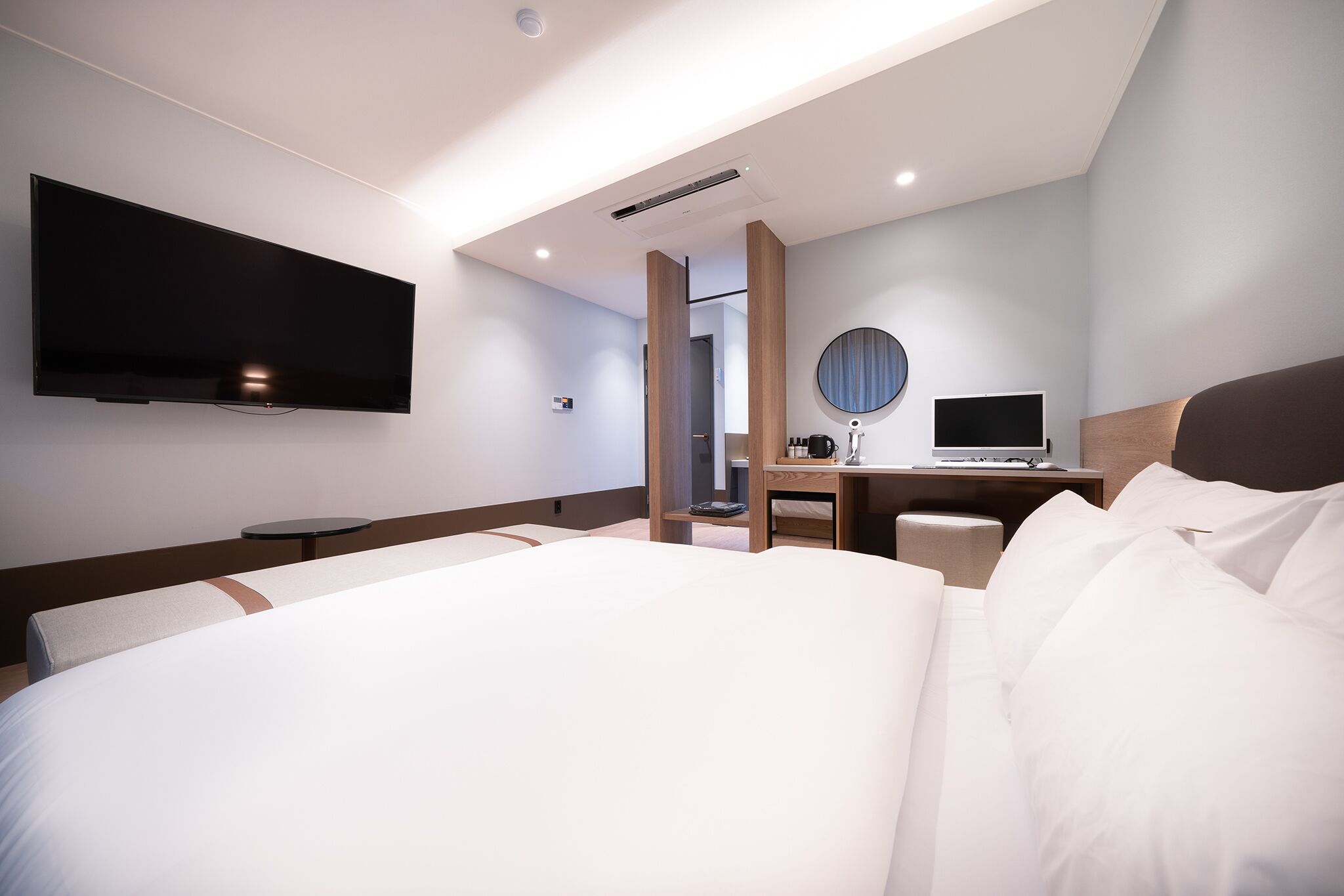 Ein modernes Hotelzimmer mit einem großen Bett, einem Schreibtisch mit einem Laptop, einem Flachbildfernseher und einem runden Spiegel.
