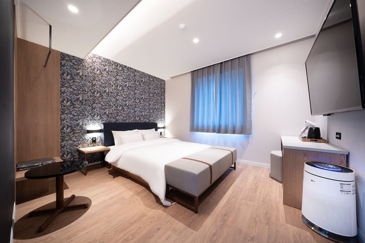 Une chambre d’hôtel moderne équipée d’un lit, d’une table de chevet, d’une lampe et d’un radiateur portatif.