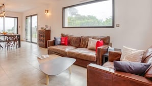 A spacious living area with a leather sofa, a coffee table, and a dining area with a wooden table and chairs. - Villa Kerhostin by Interhome (Quiberon)