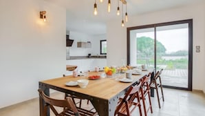 A dining area with a wooden table and chairs, a view of the outdoors through a sliding glass door, and a kitchen in the background. - Villa Kerhostin by Interhome (Quiberon)