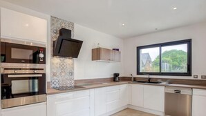 A modern kitchen with built-in appliances, a large window, and a view of greenery outside. - Villa Kerhostin by Interhome (Quiberon)