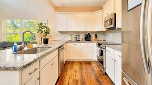 A modern kitchen with white cabinetry, granite countertops, a stainless steel refrigerator, and a wooden floor. - Hot Tub! City Side Comfort in Missionary Ridge (Chattanooga)