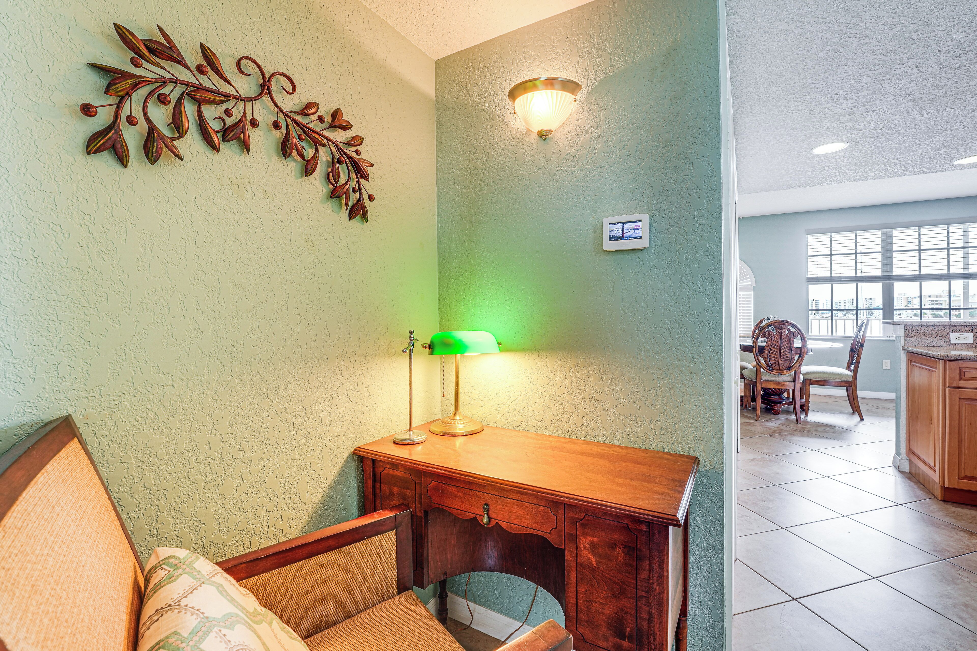A room with a wooden desk, a chair, a decorative wall piece, and a window with a view of the city.