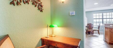 A room with a wooden desk, a chair, a decorative wall piece, and a window with a view of the city.