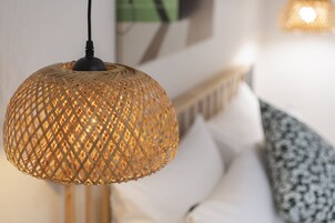 Una lámpara colgante de mimbre que cuelga del techo en una habitación con pared blanca y suelo de madera.