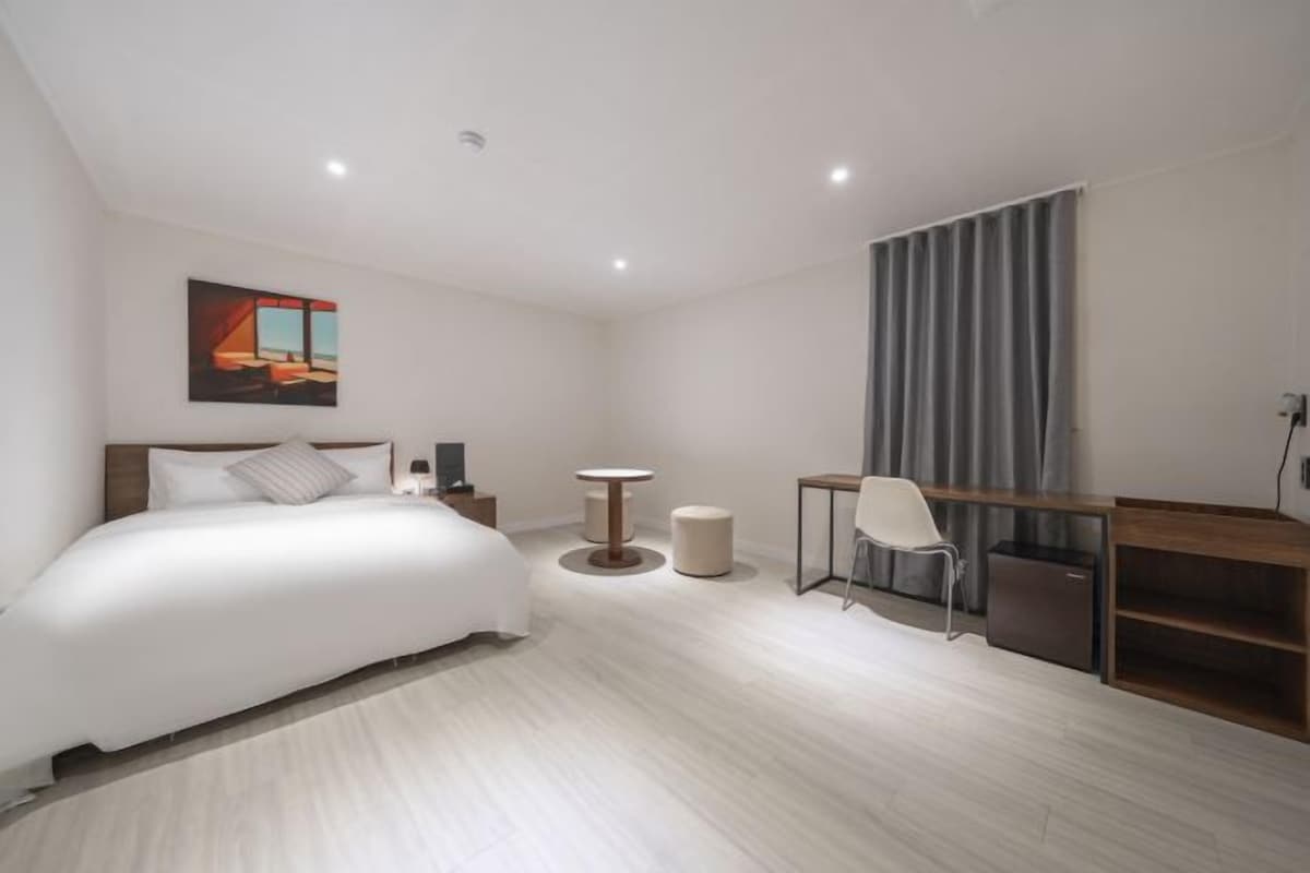 A modern hotel room with a large bed, a desk, a chair, and a small table.