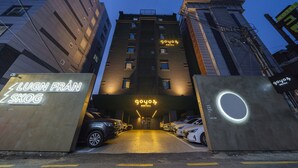 A hotel entrance with a neon sign, parked cars, and a modern building facade. - Goyo37 Hotel Osan by Anook (Osan)