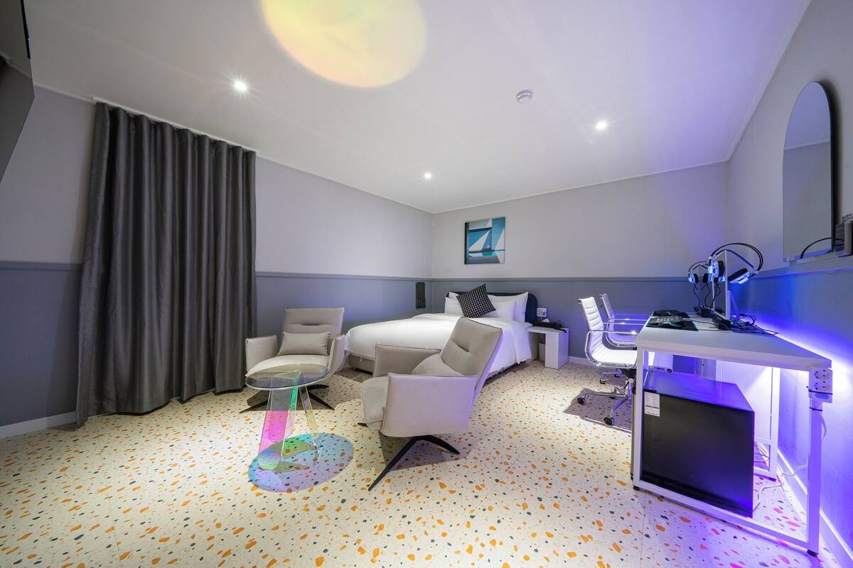 A modern hotel room with a bed, two chairs, a desk, and a computer.