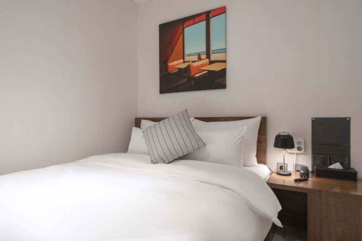 A hotel room with a bed, a nightstand, a lamp, and a painting on the wall.