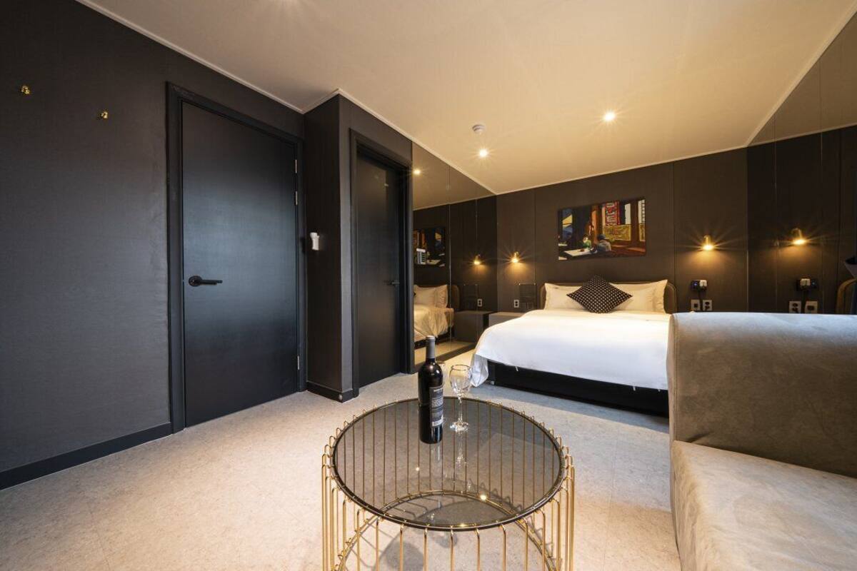 A modern hotel room with a large bed, a round glass coffee table, and a dark-colored wardrobe.