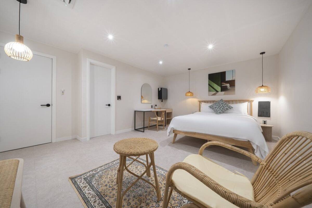 A bedroom with a bed, bedside tables, a desk, wicker chairs, and a patterned rug.