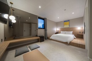 A modern hotel room with a large bed, a wooden bench, a small table, a mirror, a TV, and a window with curtains. - Goyo37 Hotel Osan by Anook (Osan)