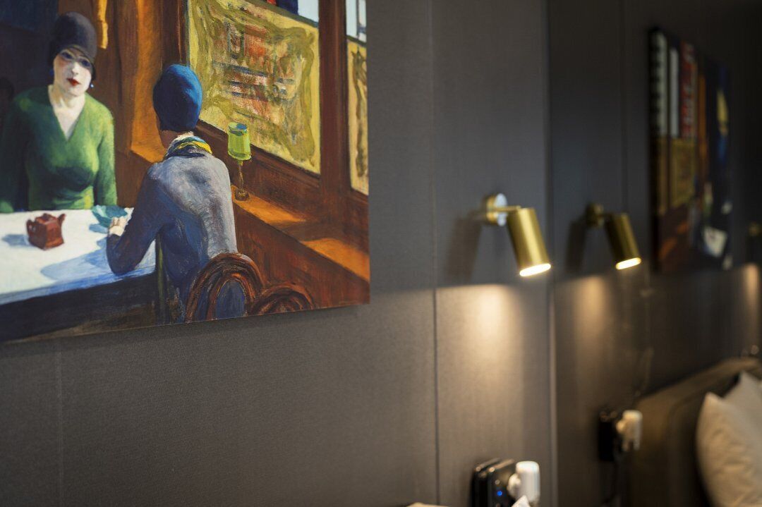 Una pintura que muestra a una pareja cenando en un restaurante, una cama con cabecero y una lámpara fijada a la pared.