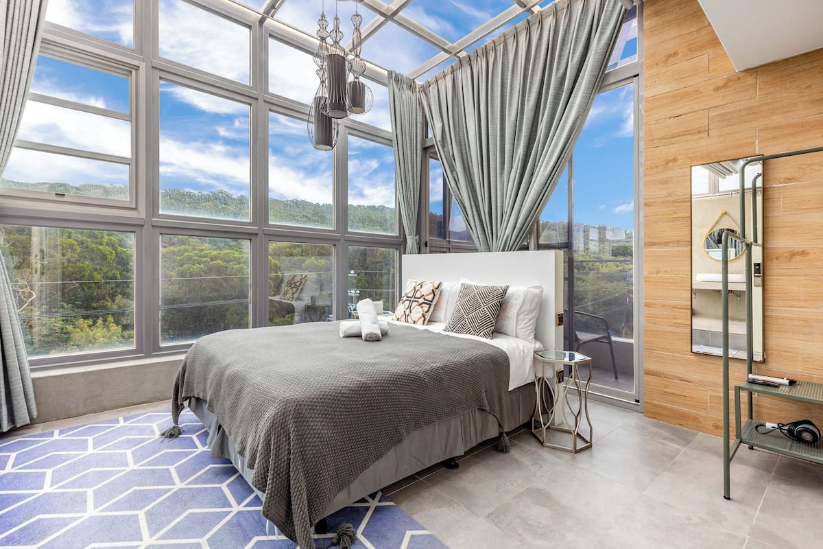 Quarto moderno com uma cama grande, vista para o exterior e parede de madeira.