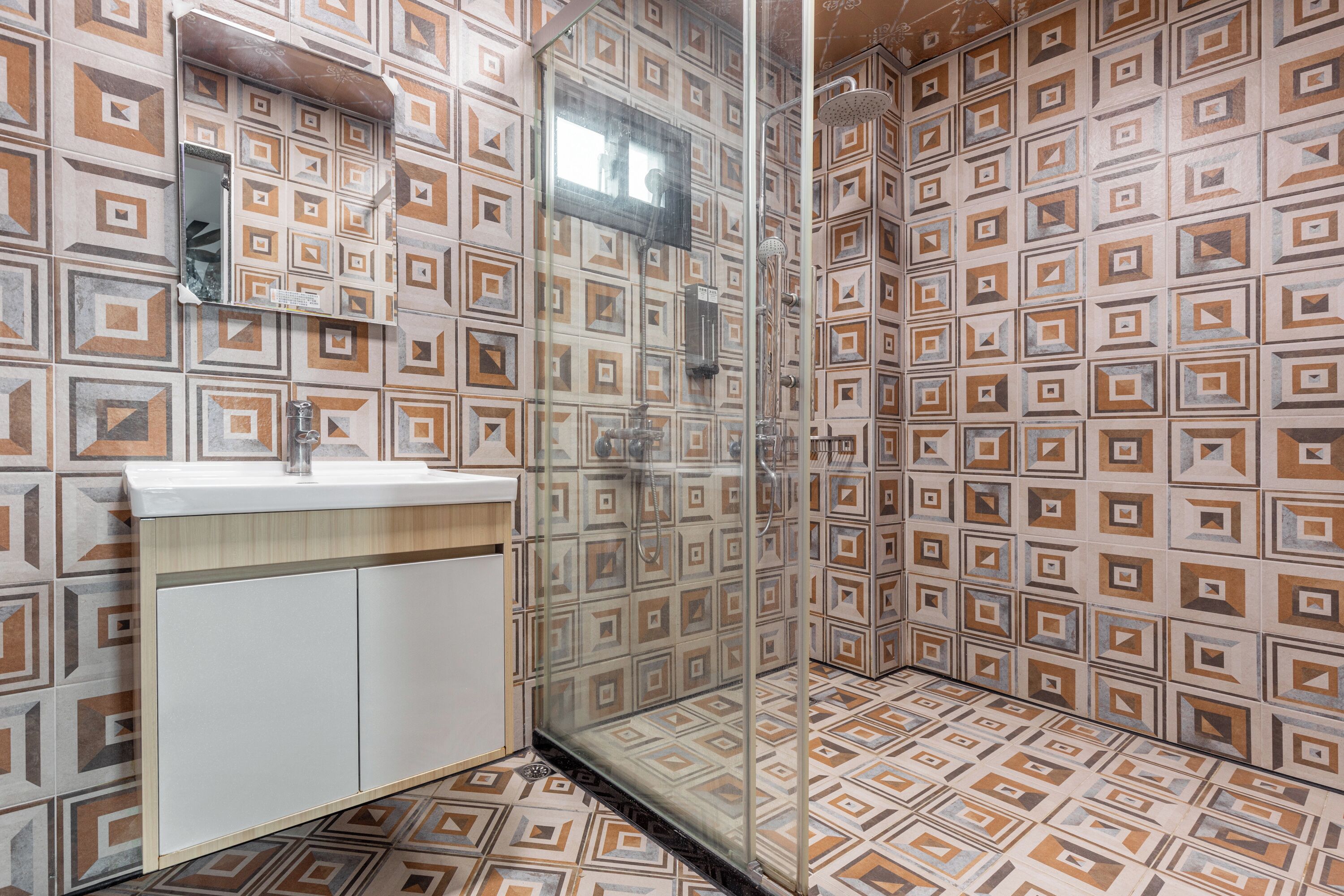 A bathroom with patterned tiles, a glass shower enclosure, and a sink with a cabinet.