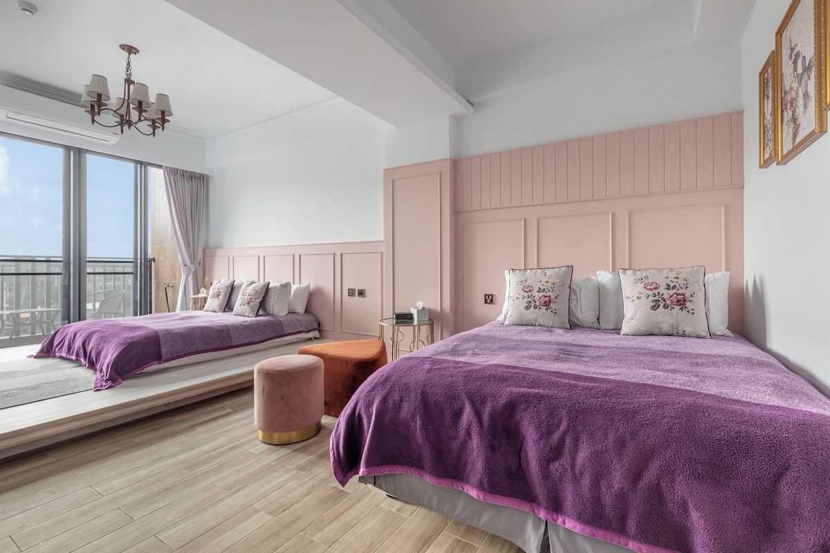 Quarto com duas camas, uma janela, um candelabro e painéis rosa na parede.