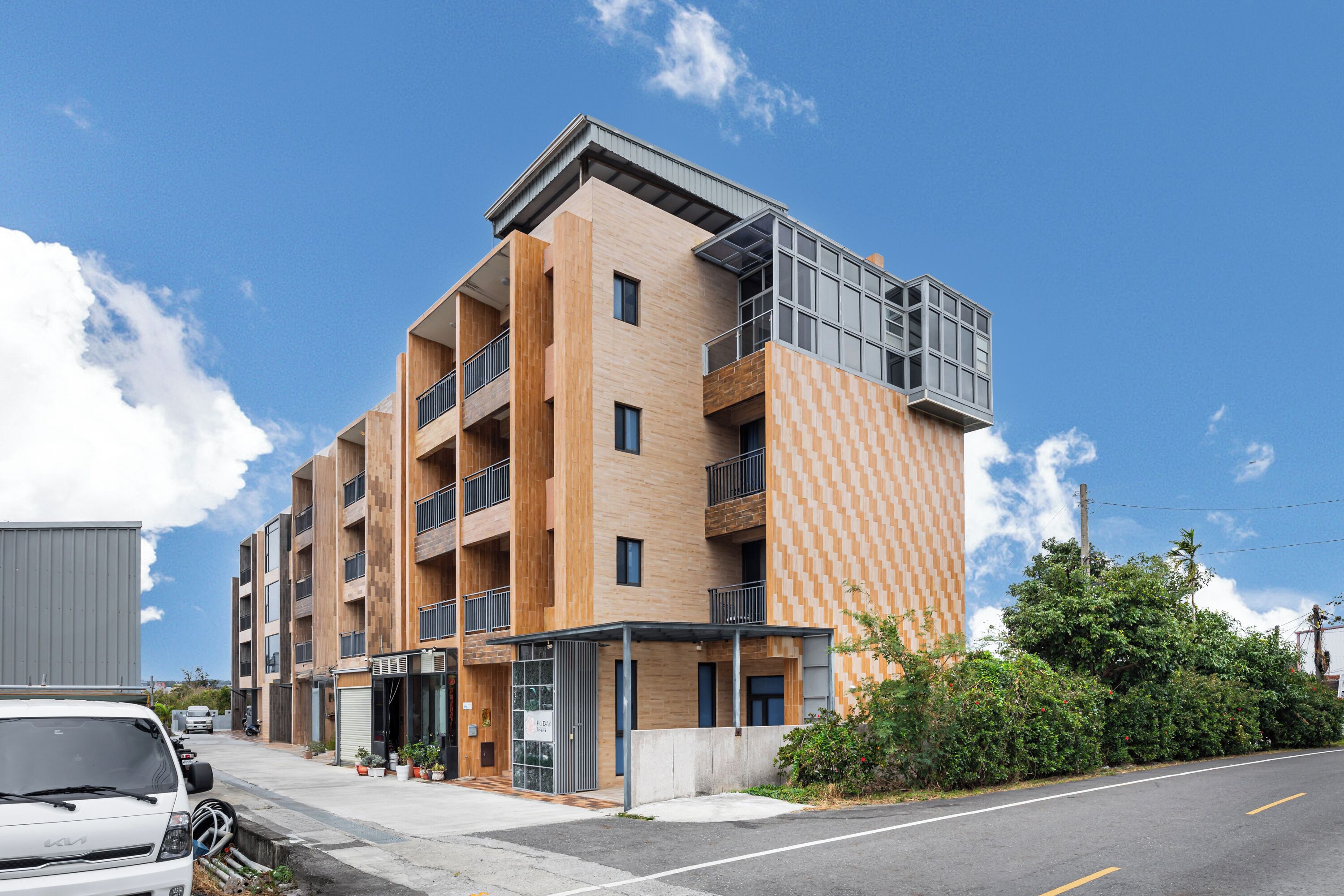 A modern multi-story building with a mix of wooden and brick facades, balconies, and a covered entrance area.