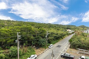 A road with vehicles, surrounded by dense greenery and hills.