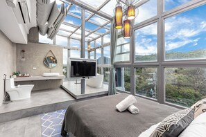 Una habitación de hotel moderna con una cama grande, un televisor, un baño con bañera y vistas a la ciudad.