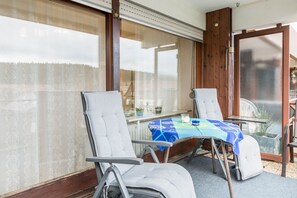 Une pièce avec une table en verre, deux chaises et une vue à travers la porte vitrée.