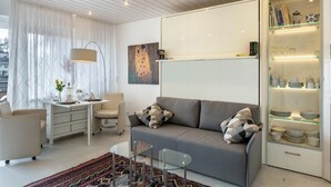 A modern living room with a sofa, a glass coffee table, a white desk, and a cabinet with glass shelves.