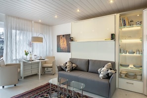 A modern living room with a sofa, a glass coffee table, a white desk, and a cabinet with glass shelves.