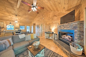 A cozy cabin interior with a living room, fireplace, and kitchen area.