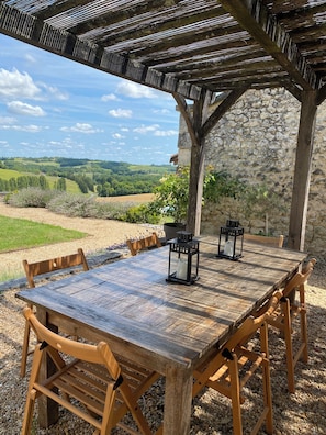 Ein Holztisch mit Stühlen unter einer Pergola, mit Blick auf eine Steinsäule und eine schöne Landschaft.