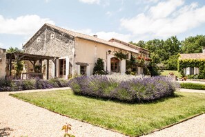 Un edificio in pietra con tetto in tegole, un portico coperto e un giardino curato con cespugli di lavanda.