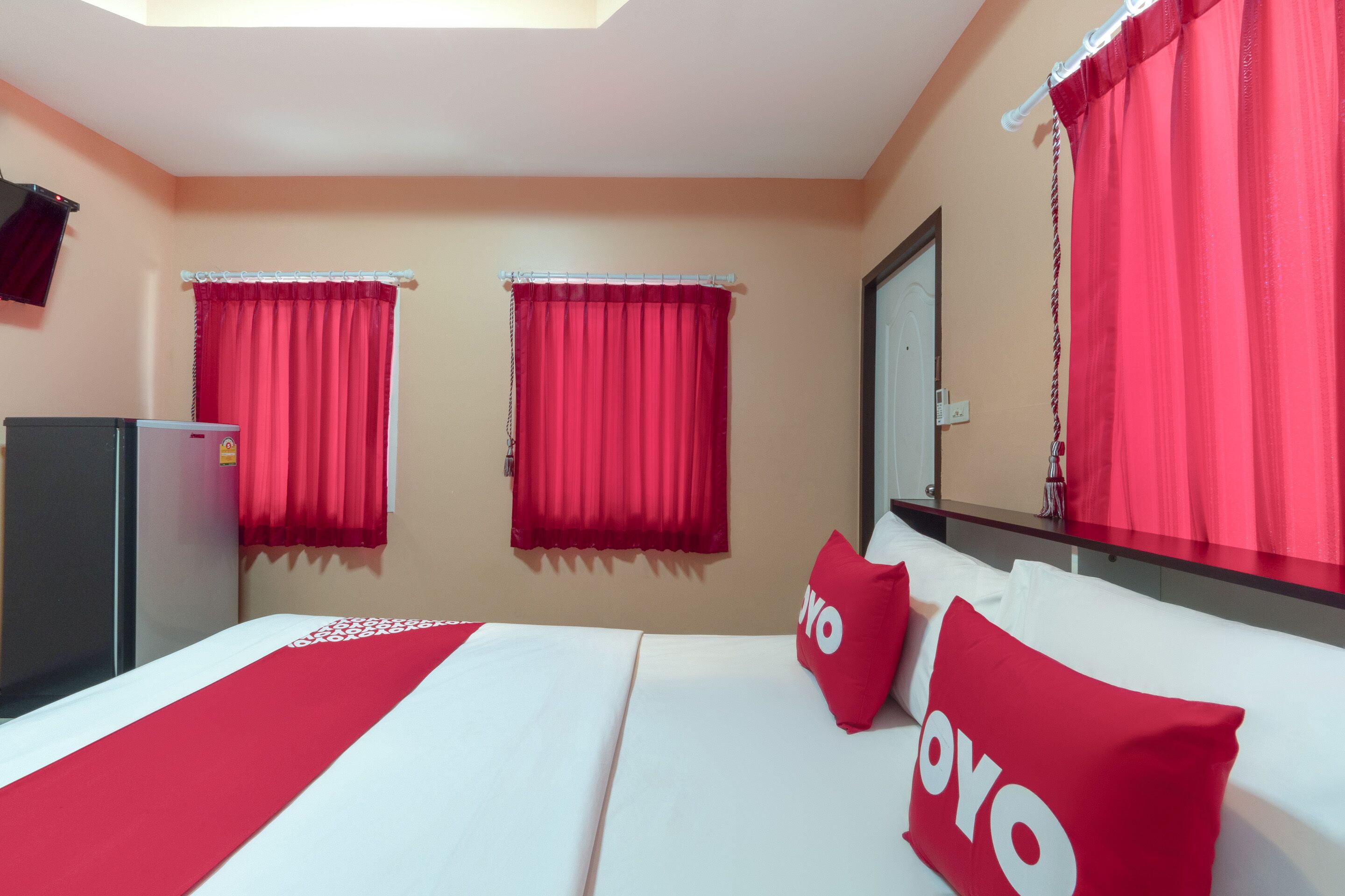 Habitación de hotel con cama, cortinas rojas, un espejo y un refrigerador.