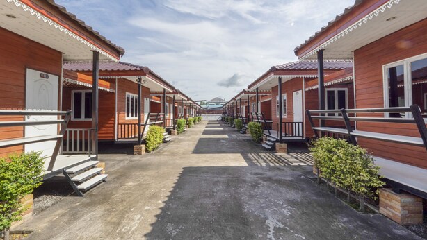 A row of wooden cabins with balconies, a central walkway, and small bushes along the path.