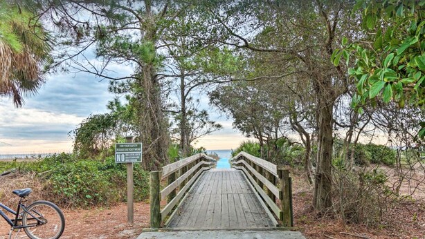 A wooden boardwalk leading to a beach, surrounded by trees and a sign advising to use footwear for safety.