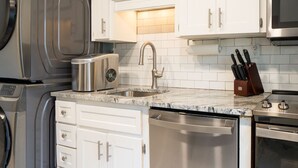 A modern kitchen with stainless steel appliances, white cabinetry, and a granite countertop.