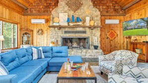 Een gezellig chaletinterieur met een stenen openhaard, houten wanden, een blauwe modulaire bank en een gestreept fauteuil.