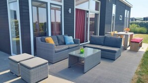 A modern outdoor living area with grey wicker furniture, a glass coffee table, and a patio table with chairs.