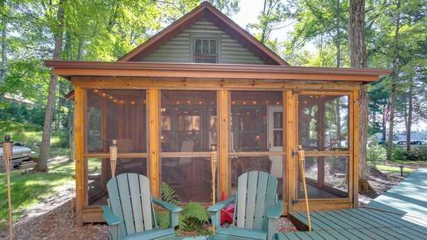 Une cabane en bois avec une véranda, deux fauteuils Adirondack et une structure vitrée.
