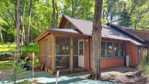 Une cabane en bois dotée d’un porche vitré, entourée d’arbres.