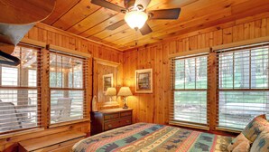Une chambre dans une cabane en bois, avec un lit, une commode et deux fenêtres équipées de stores.