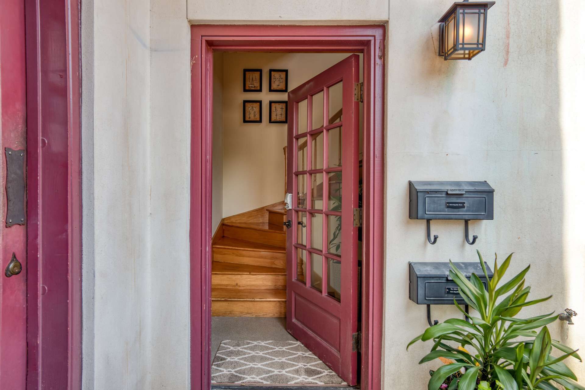 A red door leading to a staircase, a wall-mounted mailbox, and a potted plant.