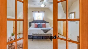 A bedroom with a bed, a ceiling fan, a window with curtains, and a wooden door.
