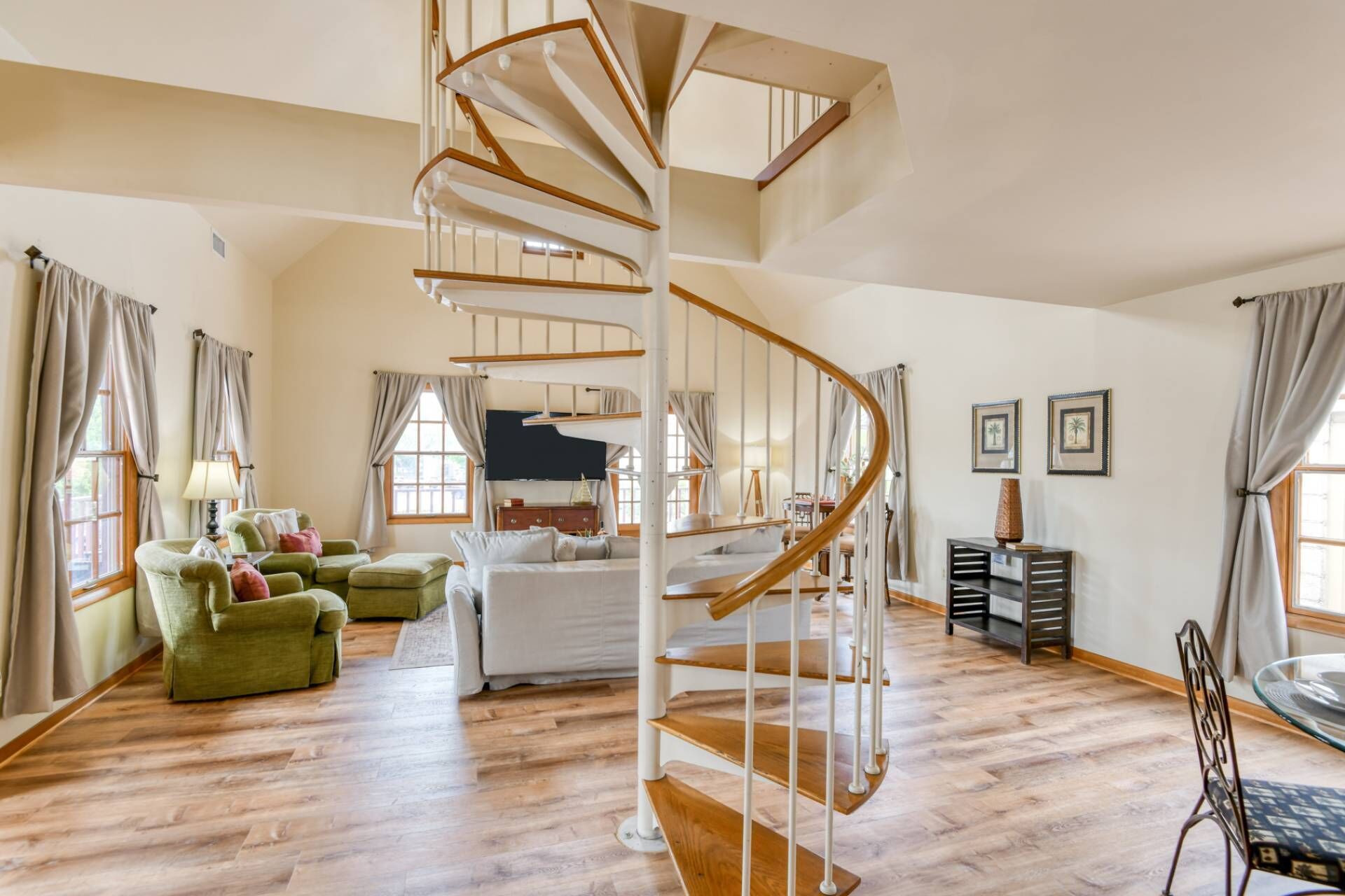 A spacious room with a spiral staircase, wooden flooring, a bed, a green armchair, and a desk with a lamp.